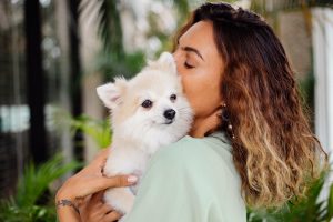 A woman gently holds a small white dog in her arms, smiling warmly at the camera.